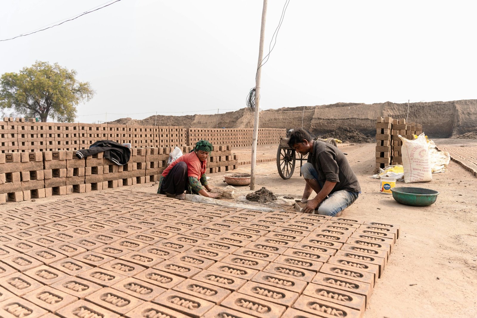 Two workers involved in traditional brick making at an outdoor kiln in India.